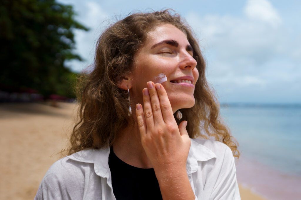 A girl applying sunblock on her face while at the beach.