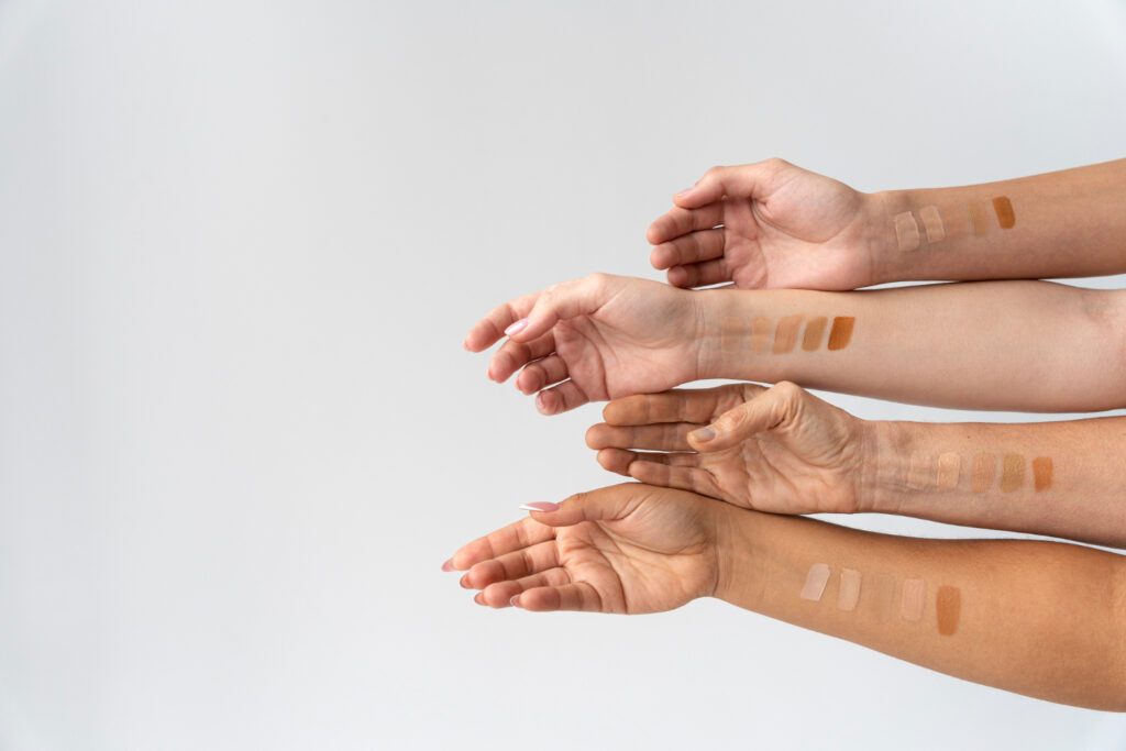 Hands of different skin tones aligned in a row with various foundation shade swatches, showcasing options for matching foundation on dusky skin tone.