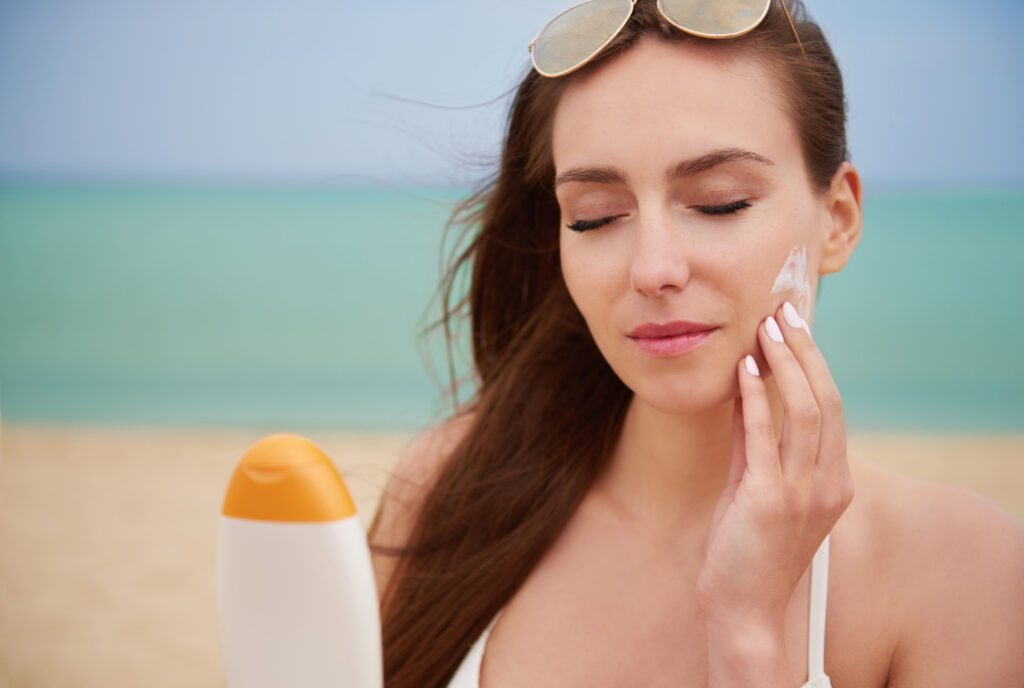 Beautiful women applying sunscreen on the beach to protect tan skin from sun damage and prevent further tanning.