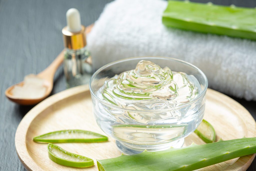 Fresh aloe vera gel in a glass bowl with a whole aloe vera leaf on a wooden plate, ideal for natural tan removal remedies and skincare treatments.